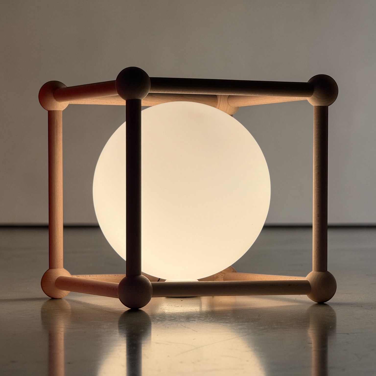 Illuminated spherical lamp held inside a simple wooden frame.